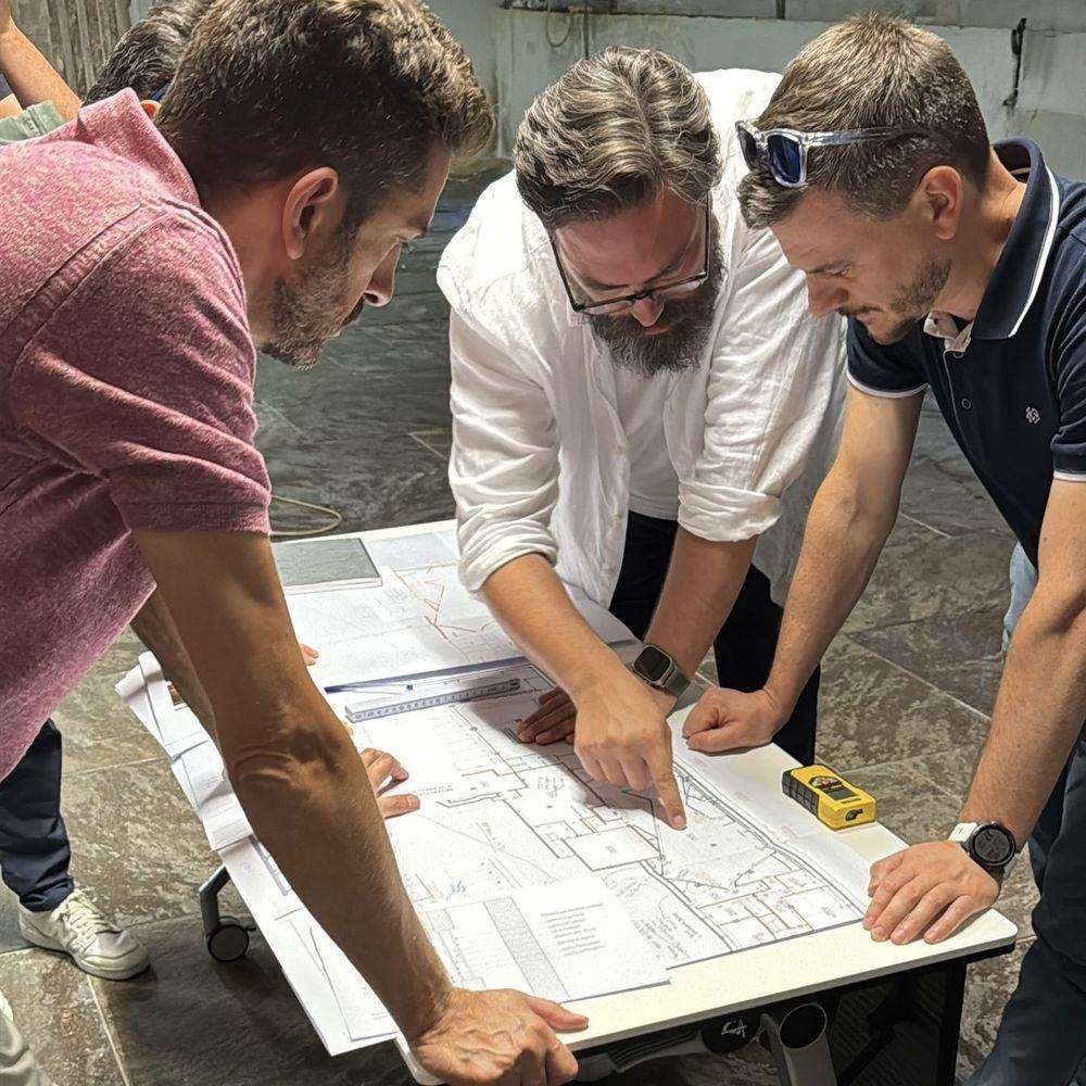 Tre persone del team studiano insieme le planimetrie di un progetto